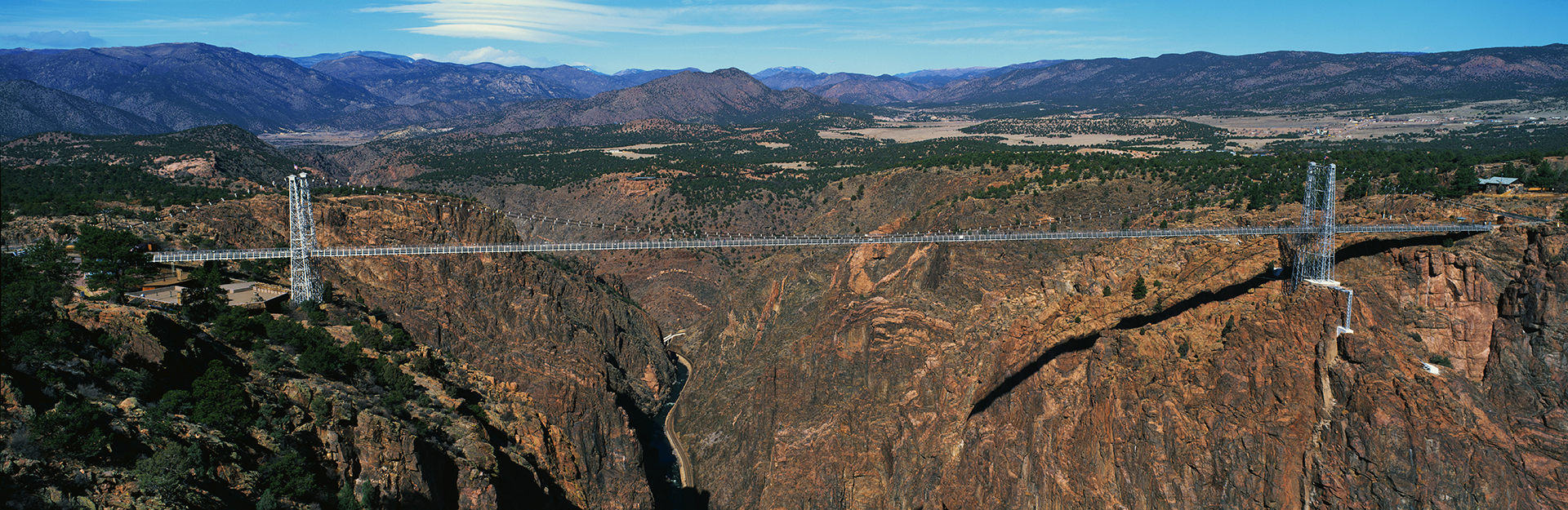 This is the Royal Gorge Bridge which is the world's highest suspension bridge. It is 1053 Ft. above the Arkansas River. Mountains are in the background with red rock below the bridge.